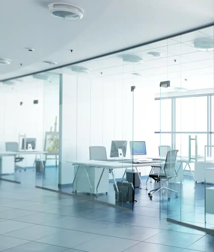 Vue lumineuse d'un bureau moderne avec des cloisons en verre, des chaises ergonomiques et des postes de travail minimalistes, mettant en avant l'agencement optimal d'un espace professionnel.