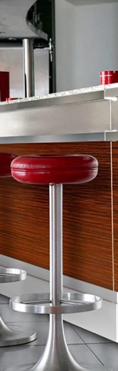 Tabouret de bureau moderne avec assise rembourrée rouge et finition métallique, placé devant un comptoir en bois élégant, idéal pour les espaces de coworking et les bureaux ouverts.