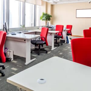 Open space coloré et fonctionnel, avec des bureaux équipés de chaises rouges ergonomiques, offrant un environnement stimulant pour le travail en équipe.