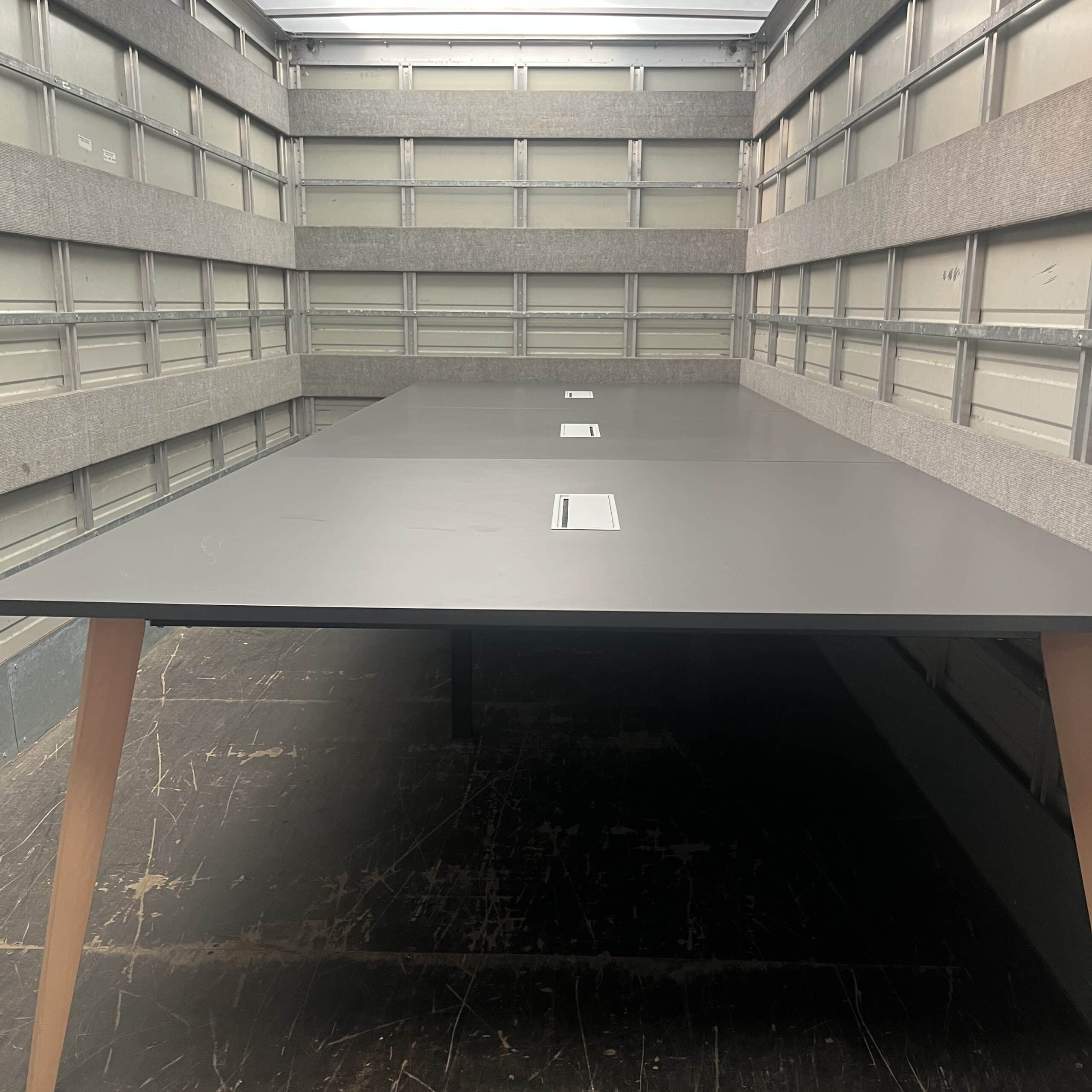 Table de réunion grise à pieds en bois disposée à l'intérieur d'un camion de transport pour mobilier de bureau.